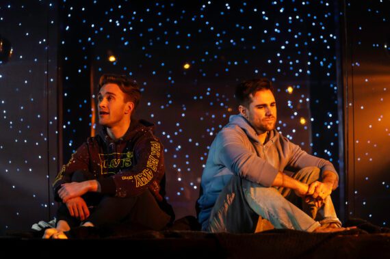 Two men sat under a starry sky on stage