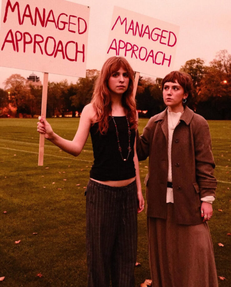 Two actors holding up picket signs with "MANAGED APPROACH" written on them.