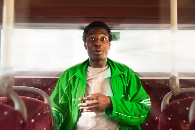 A young black man wearing a neon green sports zip up sits on the back of a bus.