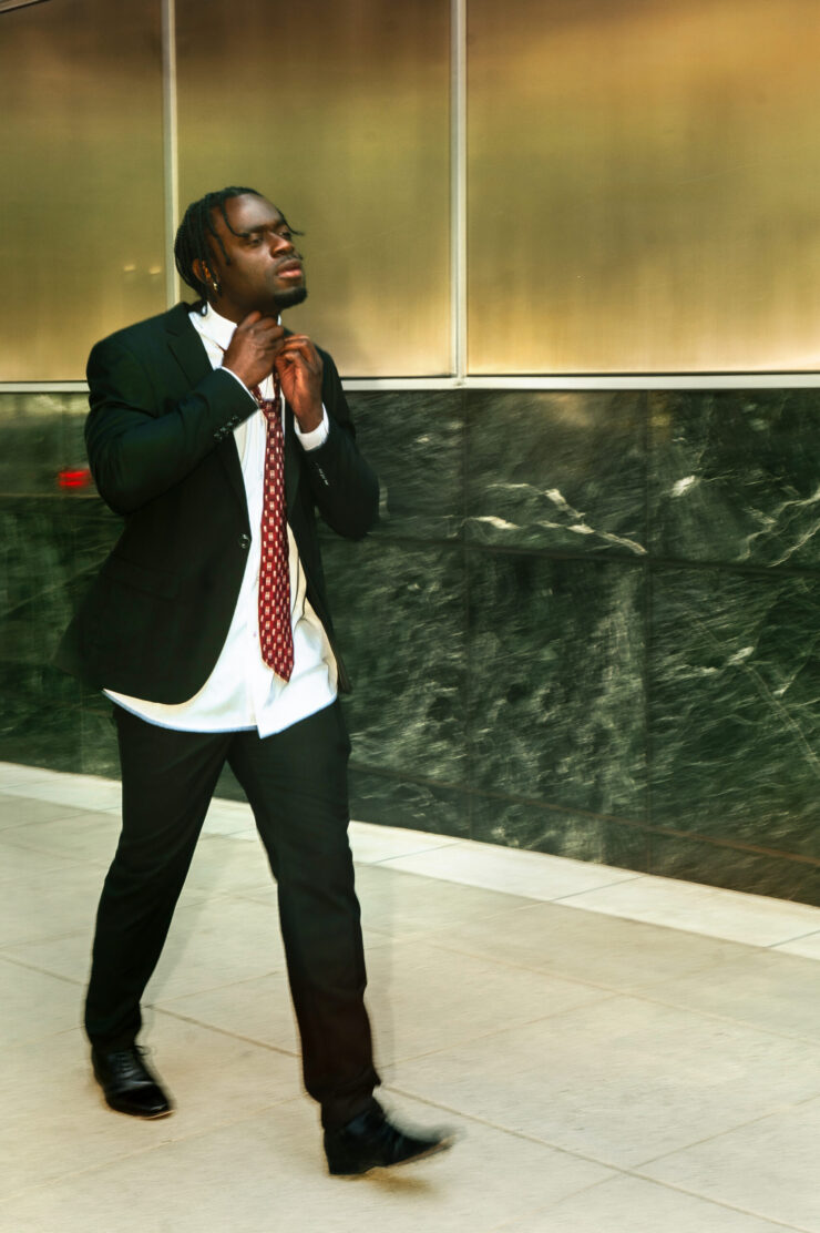 A Black man walking in a suit as he fixes his red tie.