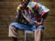 Image of Louis sitting down on a chair and his right hand on his chin.