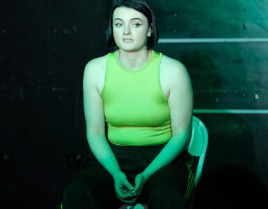 A young woman is sitting down wearing green shirt and green lighting.