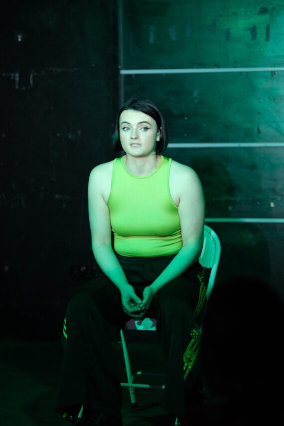 A young woman is sitting down wearing green shirt and green lighting.