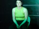 A young woman is sitting down wearing green shirt and green lighting.