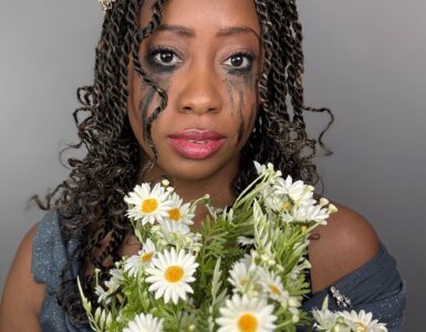 A Black woman with long twists and smudged running eyeshadow and mascara wearing a crown and holds a bouquet of flowers.