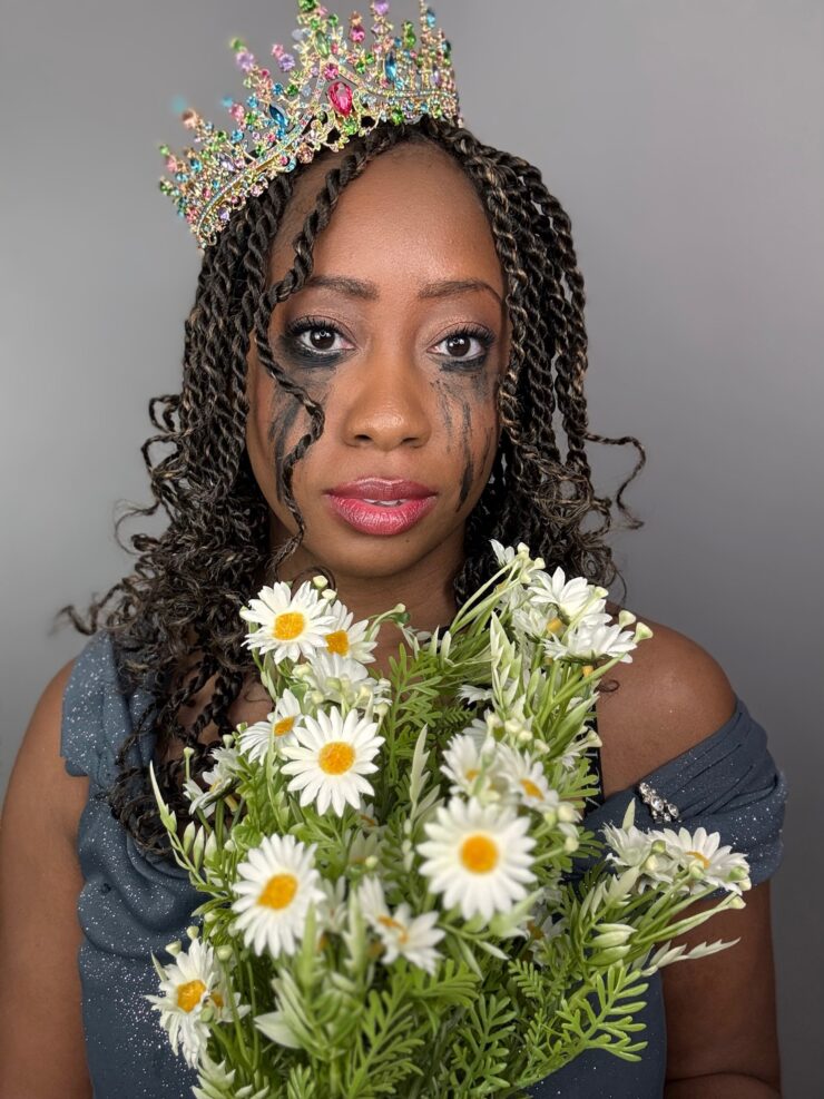 A Black woman with long twists and smudged running eyeshadow and mascara wearing a crown and holds a bouquet of flowers.