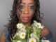 A Black woman with long twists and smudged running eyeshadow and mascara wearing a crown and holds a bouquet of flowers.
