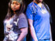 Two women face the camera their backs to each other. Woman on the left is wearing casual clothing and woman on the right wearing scrubs.